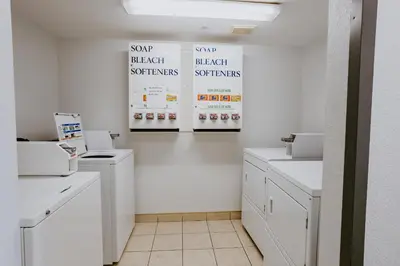 a laundry room with white cabinets and posters on the wall at Western Budget Plus Mosaic Suites in Red Deer