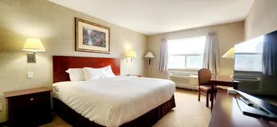 a hotel room with a bed and a desk and a television at Park Hill Inn & Suite in Red Deer