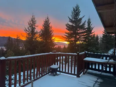 a snow covered deck with a bench and a sunset at Anglemont Inn in Anglemont