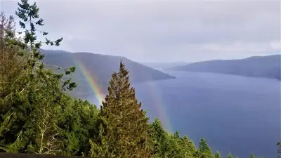 a rainbow over a body of water with trees at Moon Water Lodge in Malahat
