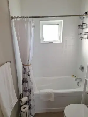 a white bathroom with a tub and a shower curtain at Two Bedroom Suite with AC, Sleeps 8- Welcome Snacks and Drinks Included in Langford