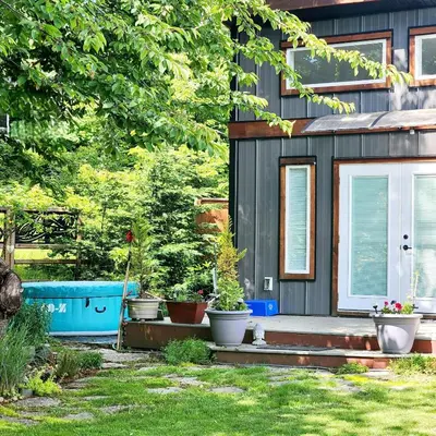 a house with a porch with pots of plants at Tiny House with Hot Tub, close to golf and skiing!! in Oyster Bay