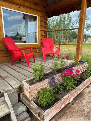 two red chairs sitting on a porch with flowers at Dry Log Cabin with Mountain Views in Upper Laberge