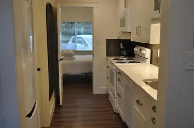 a kitchen with white cabinets and a bed in a room at Qualicum Beach Ocean Suites in Qualicum Beach