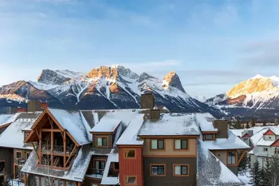 a village with snow covered mountains in the background at Magnificent Mountain Penthouse - Hot Tub & Pool managed by Little Sister Getaways in Canmore