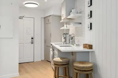 a white kitchen with a sink and two stools at KING Bed - Premium STUDIO Suite - Ski Valet - Village in Whistler