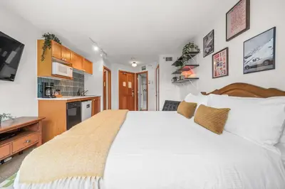 a bedroom with a large white bed and a kitchen at Mid Century Modern - Studio w Pool & Hot Tub in Whistler