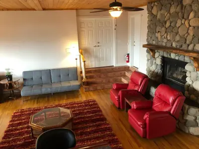 a living room with red chairs and a stone fireplace at Heated pool, hot tub, 4 AC lake view bedrooms in West Kelowna