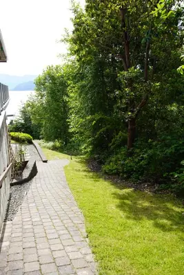 a stone path next to the water with trees at Blue House in Gibsons
