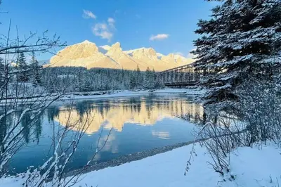 a bridge over a river with snow covered mountains at #304 Mountain View 1BR in Canmore DT in Canmore
