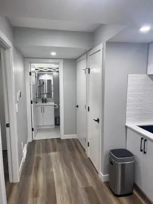 a bathroom with white walls and wooden floors and white cabinets at Adorable Private Suite in Seton SE, Calgary in Calgary