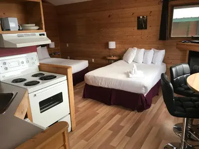 a small room with two beds and a stove at Bear Cove Cottages in Port Hardy