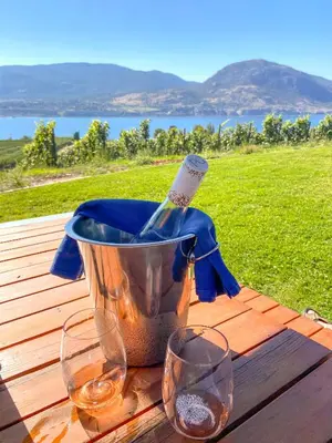 a bottle of wine in a bucket on a table with two glasses at Kelowfornia Lakeview Retreat in Kelowna