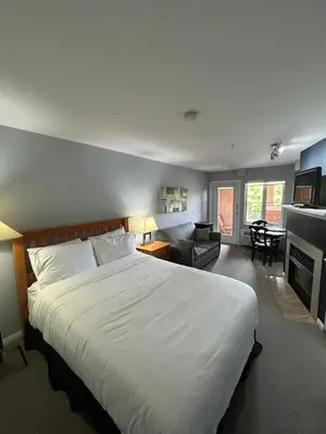 a bedroom with a large white bed and a living room at Borgata Lodge Resort in Kelowna