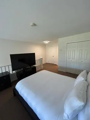 a bedroom with a large white bed and a flat screen tv at Borgata Lodge Resort in Kelowna