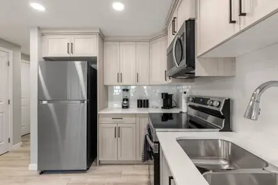 a kitchen with white cabinets and a stainless steel refrigerator at Brand New Luxury Walk-out Suite - Calgary in Calgary