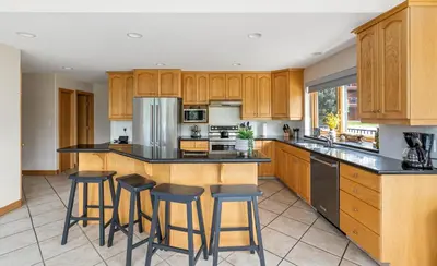 a kitchen with wooden cabinets and bar stools at Chateau Lawrence, Pool Table, Kids' Gaming Room in Fairmont Hot Springs
