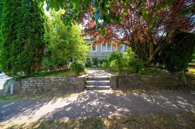 a house with a stone wall in front of a street at Charming Home Near UBC with Parking & Backyard in Vancouver
