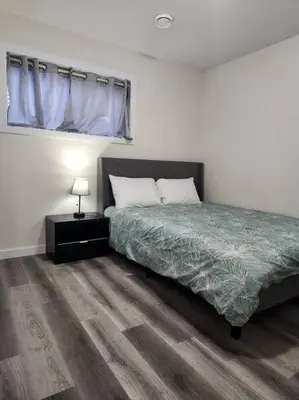 a bedroom with a bed and a lamp and a window at Modern 2 Bedroom Basement Suite Chappelle Edmonton in Edmonton