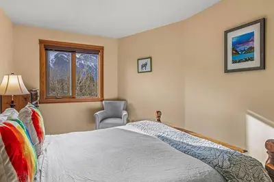 a bedroom with a bed and a chair and a window at C303 Hidden Gem with MTN andCreek View, Quiet and Private in Canmore
