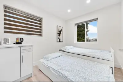 two beds in a white room with a window at Entire new small home in Vancouver