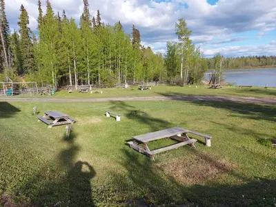 two picnic tables in a field next to a lake at Escott Bay Resort in Anahim Lake