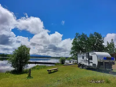 a trailer parked next to a lake with a bench at Escott Bay Resort in Anahim Lake
