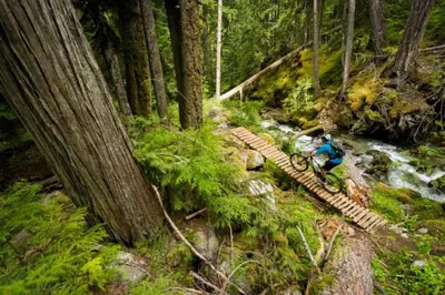 a person crossing a wooden bridge over a stream at Glacier Lodge Premiere Suite in Whistler