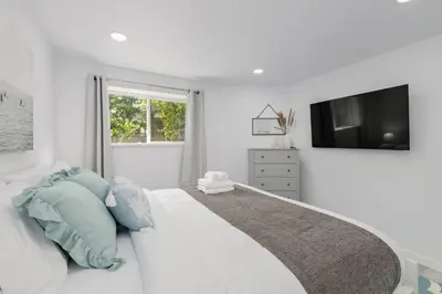 a white bedroom with a large bed with blue pillows at Serenity 1BR & 1 DEN Home at Folsom Ave in Coquitlam