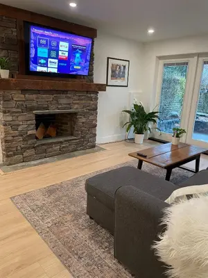 a living room with a couch and a tv on a stone fireplace at Spacious Forested Garden Suite in North Vancouver