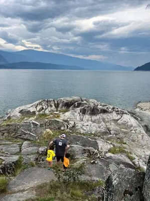 a man standing on the rocks near the water at Michaud's Basement unit in Nakusp