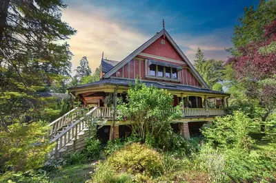 a large red house with a deck in the woods at Hummingbird Gardens B&B in Ladysmith