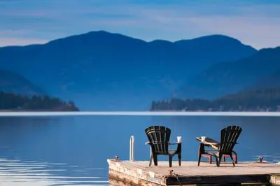 two chairs and a table on a dock near a lake at Christina Lake Lakefront, Hot Tub, Amazing Views in Christina Lake