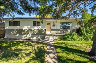 a white house with a tree in front of it at Digital Nomad's Calgary Inner City Gem 3Bd, 5Bed, Sleeps 8, Main Level in Calgary