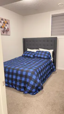 a bedroom with a bed with a blue plaid blanket at Exquisite Basement Suite, 7mins away to Landmark Cinema and Malls in Calgary
