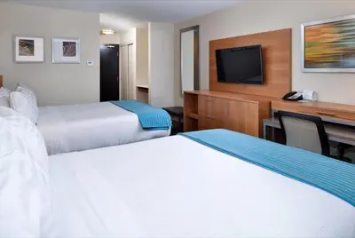 a hotel room with two beds and a desk with a television at Holiday Inn Hotel & Suites Edmonton Airport Conference Centre by IHG in Nisku