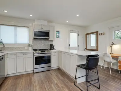 a kitchen with white cabinets and a table and chairs at Fairfield Estate Coach House - 30-Day Stay, steps from Cook Street Village by Victoria Prime! in Victoria