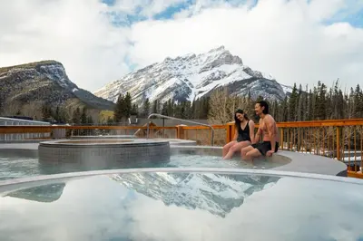a man and woman sitting in a pool with a mountain at Otter Hotel in Banff