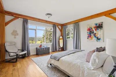 a bedroom with a bed and a chair and windows at Rolling Hills Retreat - Family Friendly in Millarville