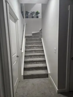 a hallway with a staircase with white walls and carpet at Wola's Place in Calgary