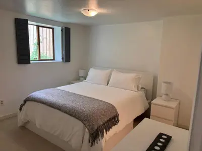 a white bedroom with a bed and a window at Bright Garden Suite Across From Park in Kitsilano in Vancouver