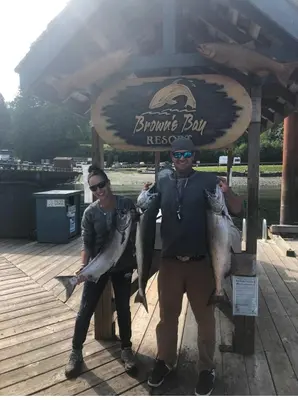 two men holding up fish in front of a sign at Brickwood Cabin in Sayward