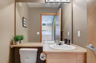 a bathroom with a sink and a toilet and a mirror at Cozy Condo with Epic Mountain Views, Parking, Air Con in Canmore
