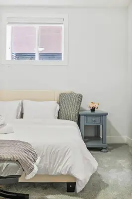 a bedroom with a bed and a table with a window at Bright & Cozy 2-Bedroom Basement Suite in Chestermere