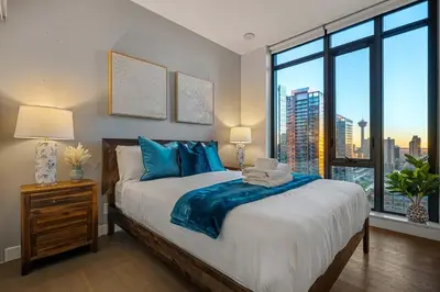 a bedroom with a large bed with a large window at Poolside Bliss - 22 FL w Tower Views! FREE Banff Pass, Gym, Parking, Summer Outdoor Pool! in Calgary
