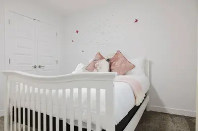 a white crib in a white bedroom with pink pillows at Executive Modern Family Haven for Short Stays in Edmonton