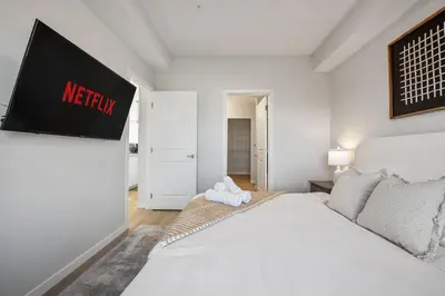 a white bedroom with a bed and a tv on the wall at Very Spacious Luxury Apartment with AC, 70