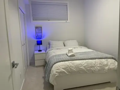 a white bedroom with a bed and a blue light at A Cozy Private Suite in Rangeview, SE Calgary in Calgary