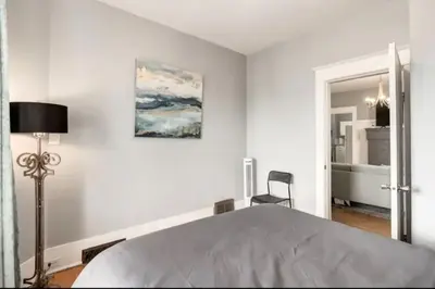 a white bedroom with a bed and a chair at Ceruleans 3BR Suite in Calgary in Calgary