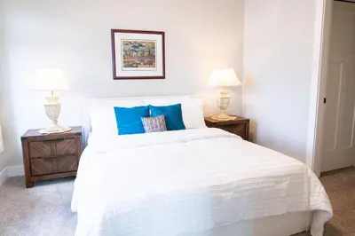 a bedroom with a white bed with two lamps at The Luna, New Penthouse w Patio, Lake and Mtn Views in Harrison Hot Springs